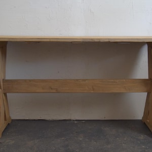 May include: A light brown wooden table with a rectangular top and cross-shaped legs. The table is made of natural wood and has a simple, rustic design. The table is approximately 60 inches long.