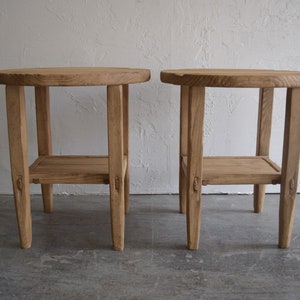 May include: Two wooden side tables with a round top and a lower shelf. The tables are made of light brown wood and have a rustic look.