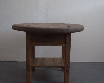 May include: A rustic wooden side table with a round top, a single drawer, and a lower shelf. The table is made of dark brown wood and has a distressed finish.