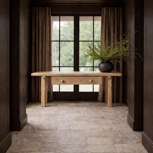 May include: A hallway with a light wood table featuring two drawers, a dark metal vase with greenery, and a large window with brown curtains. The walls and ceiling are dark brown, and the floor is stone tile.