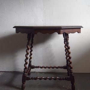 May include: A dark brown antique side table with a scalloped edge and spiral-turned legs. The table has a rectangular top and a lower shelf, showcasing a classic design. The wood has a rich, warm tone, adding to its vintage appeal.