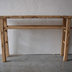 May include: A rustic wooden console table with a single shelf. The table has a natural wood finish and is made of reclaimed wood.