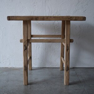 May include: A rustic wooden table with a square top and a simple, open frame design. The table is made of natural wood with a light brown finish and has a distressed look.