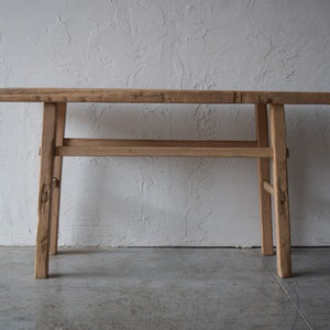 May include: A rustic wooden console table with a single shelf. The table has a natural wood finish and is made of reclaimed wood.