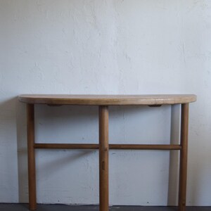 May include: A wooden half-round console table with a natural finish. The table has a single shelf and four legs.