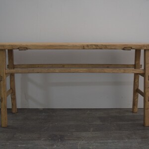 May include: A rustic wooden console table with a natural finish. The table has a rectangular top and a simple, open frame with two horizontal supports. The table is made of reclaimed wood and has a distressed look.