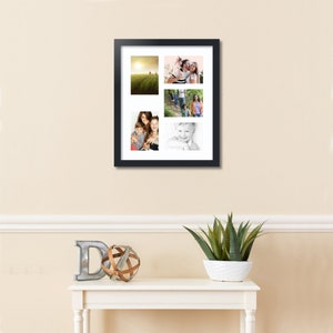 May include: A black picture frame with a white mat and four photos of a family. The photos are arranged in a grid pattern. The frame is hanging on a light beige wall.