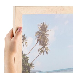 May include: A framed photograph of a tropical beach scene with palm trees and a blue sky. The frame is made of natural wood.