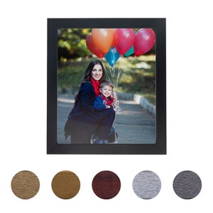 May include: A black picture frame with a photo of a woman and a child holding balloons. The woman is wearing a black jacket and a red scarf. The child is wearing a red shirt and blue jeans. The balloons are red, orange, blue, and green.