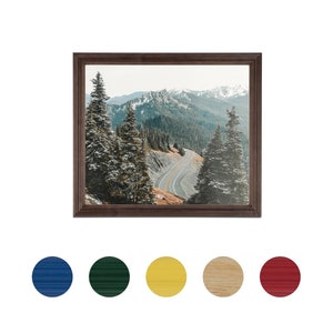 May include: A framed photograph of a winding road through a snowy mountain landscape. The road is surrounded by evergreen trees and the mountains are covered in snow.