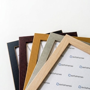 Puede incluir: Una colecci&oacute;n de marcos de fotos rectangulares dispuestos en abanico, con varios acabados de grano de madera en negro, marr&oacute;n oscuro, amarillo dorado, gris claro y madera clara natural, cada uno con papel blanco con el texto ArtToFrames.