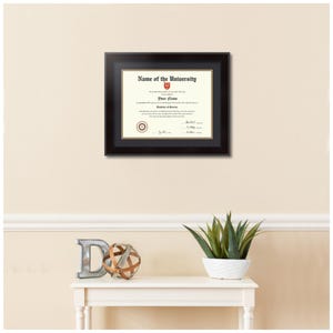 May include: A black framed diploma with a gold mat, hanging on a beige wall. The diploma is for "Your Name" and is from "Name of the University".