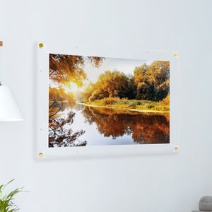 May include: A framed photograph of a river scene with fall foliage reflected in the water. The frame is clear acrylic with gold-colored mounting hardware.