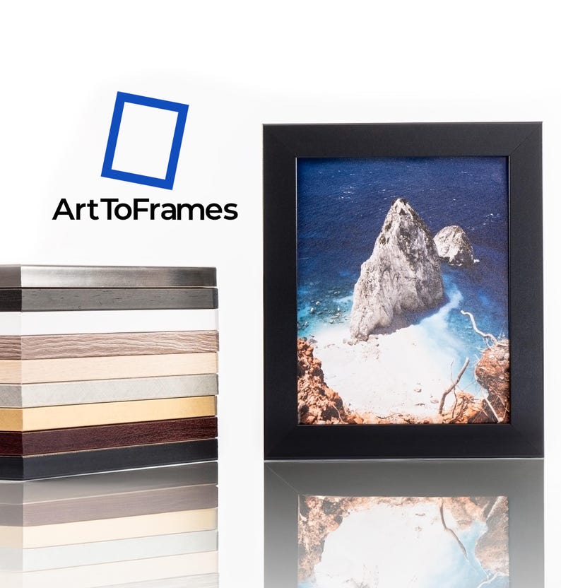 Puede incluir: Un marco de fotos negro que contiene una fotograf&iacute;a de un paisaje costero rocoso con agua azul, colocado junto a una pila vertical de muestras de marcos en diferentes colores y texturas, con el logotipo de ArtToFrames visible arriba.