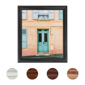 May include: A framed photograph of a building with a teal door and shutters. The building is painted a light yellow with a pink trim. The door has a glass panel and a small window above it.