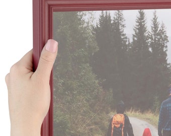 May include: A red wood picture frame with a photo of a family walking on a path in a forest. The photo is slightly blurred.