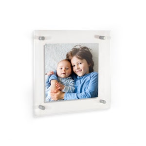 May include: A clear acrylic frame with a photo of two siblings. The older sibling is holding the younger sibling. Both siblings are smiling.
