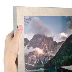 Puede incluir: Un marco de fotos rectangular con un acabado plateado texturizado que contiene una fotograf&iacute;a de paisaje de una cordillera, un bosque y un lago. El marco tiene un dise&ntilde;o de esquinas en inglete y un brillo met&aacute;lico en toda su superficie.