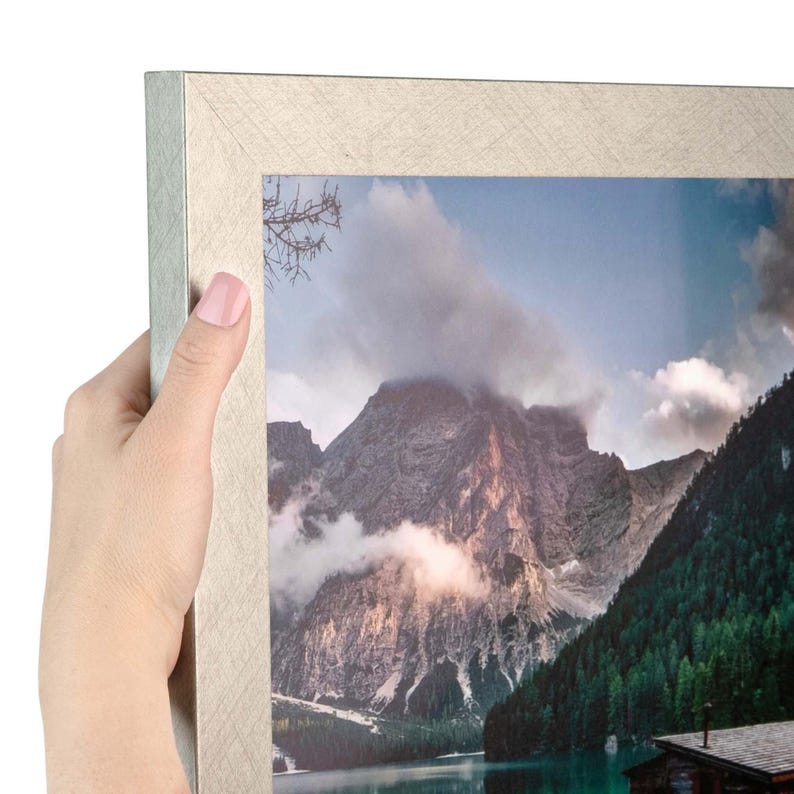 Puede incluir: Un marco de fotos rectangular con un acabado plateado texturizado que contiene una fotograf&iacute;a de paisaje de una cordillera, un bosque y un lago. El marco tiene un dise&ntilde;o de esquinas en inglete y un brillo met&aacute;lico en toda su superficie.