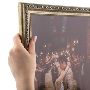 May include: A gold-toned picture frame with a wedding photo inside. The photo shows a couple kissing with sparklers in the background.