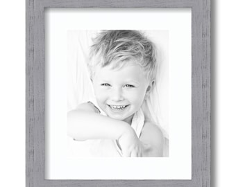 May include: A grayscale framed photograph of a smiling child. The frame is a weathered gray with a textured appearance. The photograph is centered within a white mat, showcasing the child's face and upper body.