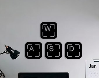 May include: A black desk with a white chair, a computer monitor, a black and white clock displaying 2:18, a black filing cabinet, and a black lamp. The wall behind the desk has black keyboard keys with the letters W, A, S, and D on them. A calendar showing the month of January is hanging on the wall.