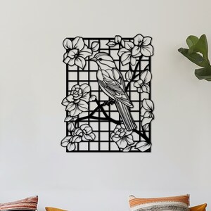 May include: Black metal wall art featuring a bird perched on a branch with flowers. The bird and flowers are cut out of the metal, creating a delicate and intricate design.