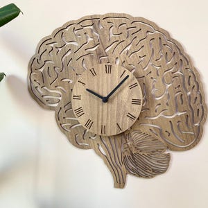 Puede incluir: Un reloj de pared de madera con forma de cerebro humano con n&uacute;meros romanos en la esfera.