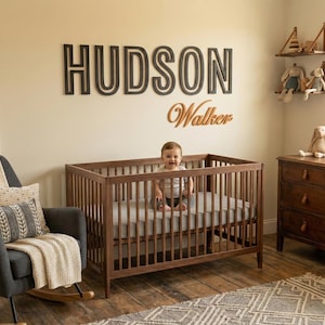 Puede incluir: Una escena de guarder&iacute;a con una cuna de madera, un sill&oacute;n mecedora gris oscuro y una c&oacute;moda de madera. El nombre "HUDSON" se muestra en la pared sobre la cuna, con "Walker" debajo. Un beb&eacute; est&aacute; en la cuna.
