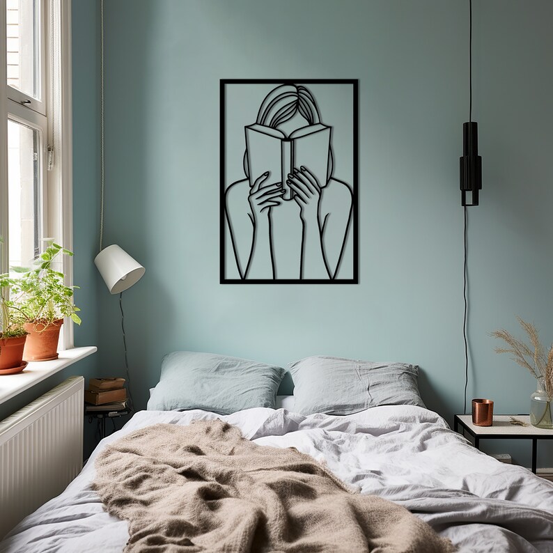 Puede incluir: Arte de pared de metal negro que representa a una persona leyendo un libro. El arte est&aacute; enmarcado en un cuadrado negro y est&aacute; montado en una pared azul claro.
