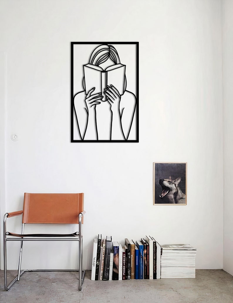 Puede incluir: Decoraci&oacute;n de pared de arte de l&iacute;nea en blanco y negro de una persona leyendo un libro. El arte est&aacute; enmarcado en un marco negro y est&aacute; colgado en una pared blanca.