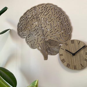 Puede incluir: Un reloj de pared de madera con forma de cerebro humano con n&uacute;meros romanos en la esfera.