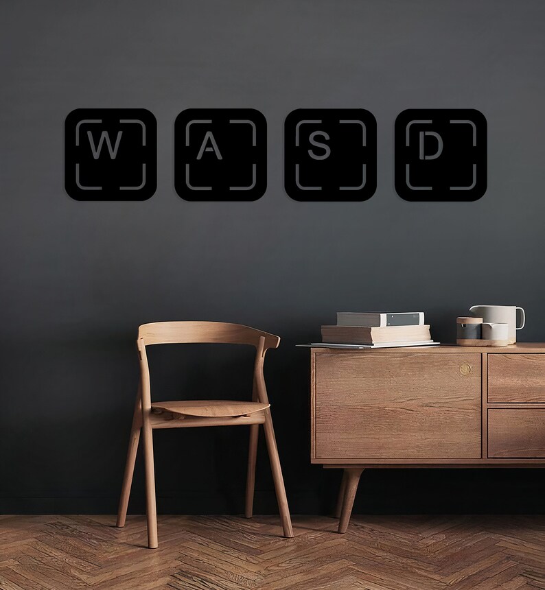 May include: Black and white keyboard keys with the letters W, A, S, and D on a grey wall. A wooden chair and a wooden cabinet with drawers are in the background.
