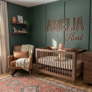 Puede incluir: Una guarder&iacute;a con una cuna de madera, una c&oacute;moda y una mecedora. Las paredes est&aacute;n pintadas de verde oscuro y la habitaci&oacute;n est&aacute; decorada con estanter&iacute;as de madera y una alfombra. El nombre "Amelia Hart" se muestra en la pared.