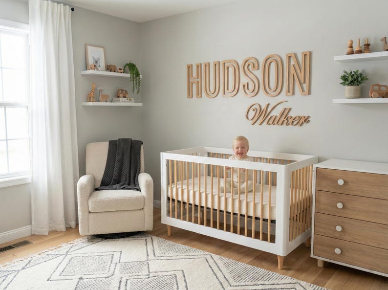 Puede incluir: Un cuarto de beb&eacute; con una cuna blanca, un sill&oacute;n beige y una c&oacute;moda de madera. La pared presenta un letrero de madera que dice "HUDSON Walker". Un beb&eacute; est&aacute; en la cuna. Estantes decorativos con juguetes y plantas.