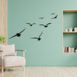 Puede incluir: Una pared verde claro con un conjunto de calcoman&iacute;as de p&aacute;jaros en silueta negra. Los p&aacute;jaros vuelan en diferentes direcciones. Hay una unidad de estanter&iacute;a de madera en la pared con algunos libros y una peque&ntilde;a planta en la estanter&iacute;a.