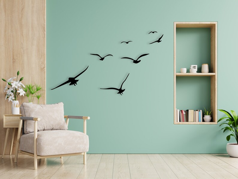 Puede incluir: Una pared verde claro con un conjunto de calcoman&iacute;as de p&aacute;jaros en silueta negra. Los p&aacute;jaros vuelan en diferentes direcciones. Hay una unidad de estanter&iacute;a de madera en la pared con algunos libros y una peque&ntilde;a planta en la estanter&iacute;a.