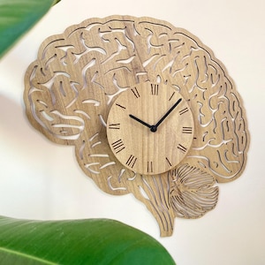 Peut inclure: Une horloge murale en bois en forme de cerveau humain avec un cadran d'horloge au centre. Le cadran de l'horloge a des chiffres romains et des aiguilles noires.