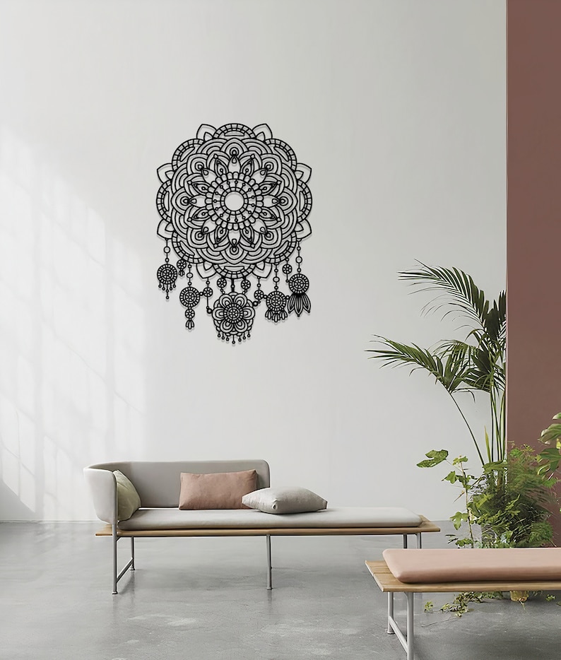May include: Black metal wall decor featuring a large mandala design with intricate details and dangling charms. The mandala is surrounded by a white wall and a light grey sofa with cushions.