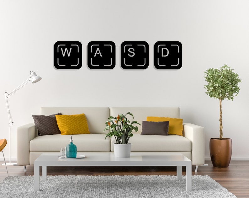 May include: Four black square wall decals with white letters spelling out "WASD" on a white wall. The decals are in a living room setting with a white sofa, a coffee table, and a potted plant.