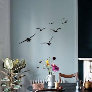 Puede incluir: Un comedor con una mesa y sillas negras. La pared est&aacute; pintada de un color azul claro y presenta una bandada de p&aacute;jaros de metal negro en vuelo. Una planta en maceta se encuentra en el suelo junto a la mesa.