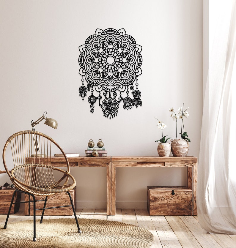 May include: Black metal wall decor featuring a large mandala design with intricate details and dangling beads. The decor is mounted on a white wall above a wooden desk with a chair.