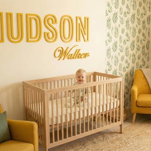 Puede incluir: Una escena de guarder&iacute;a con una cuna de madera y un beb&eacute; dentro. Encima de la cuna, el nombre "HUDSON" y el nombre "Walker" se muestran en letras amarillas. La habitaci&oacute;n tiene sillones amarillos y un papel pintado con estampado de hojas verdes y blancas.