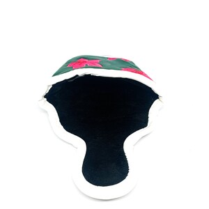 May include: A dark green golf club head cover with embroidered pink floral designs. The cover has a white trim and a black interior. The cover is designed to protect golf clubs.
