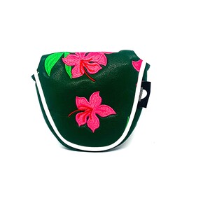 May include: Dark green golf putter cover with embroidered pink hibiscus flowers and green leaves. The cover has a white trim and a small black tag on the side.