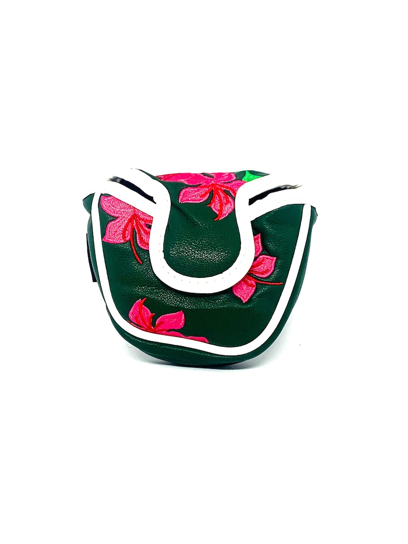 May include: Dark green golf putter cover with a white border and a vibrant pink floral design. The cover is made of a textured material and has a magnetic closure. The putter cover is designed to protect the golf club head.