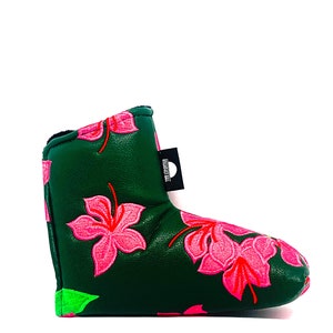 May include: A dark green golf club head cover with embroidered pink hibiscus flowers and red accents. The cover has a black tag with white text. The bottom edge is trimmed with neon green.