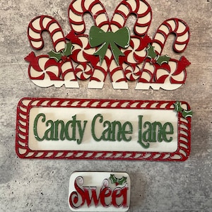 May include: Red and white candy cane lane sign with green holly and a red and white candy cane bow.  The sign reads "Candy Cane Lane".  A smaller sign reads "Sweet" with a green holly sprig.