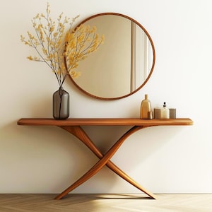 May include: A modern wooden console table with a unique crossed-leg design. A round mirror with a wooden frame hangs above the table. A vase with yellow branches and decorative bottles are on the table.