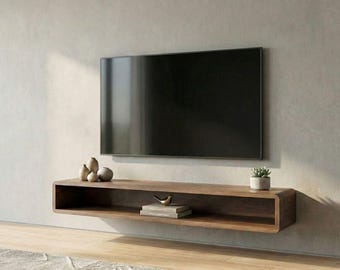 May include: A rectangular, wall-mounted wooden media console with rounded edges. The console features an open shelf containing a small metallic bird figurine, two stacked books, and a small potted succulent plant on the top surface.